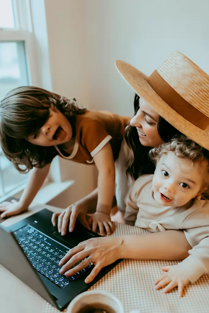 mom working on laptop with kids crawling on her