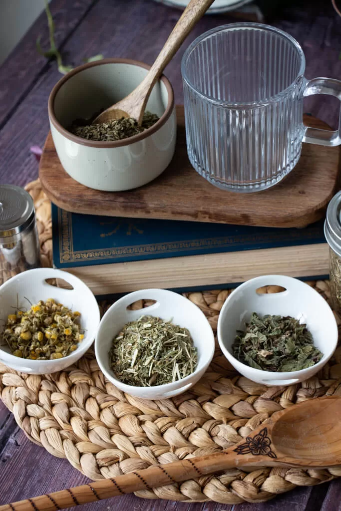 headache tea ingredients in bowls: peppermint, chamomile, feverfew, and lemon balm