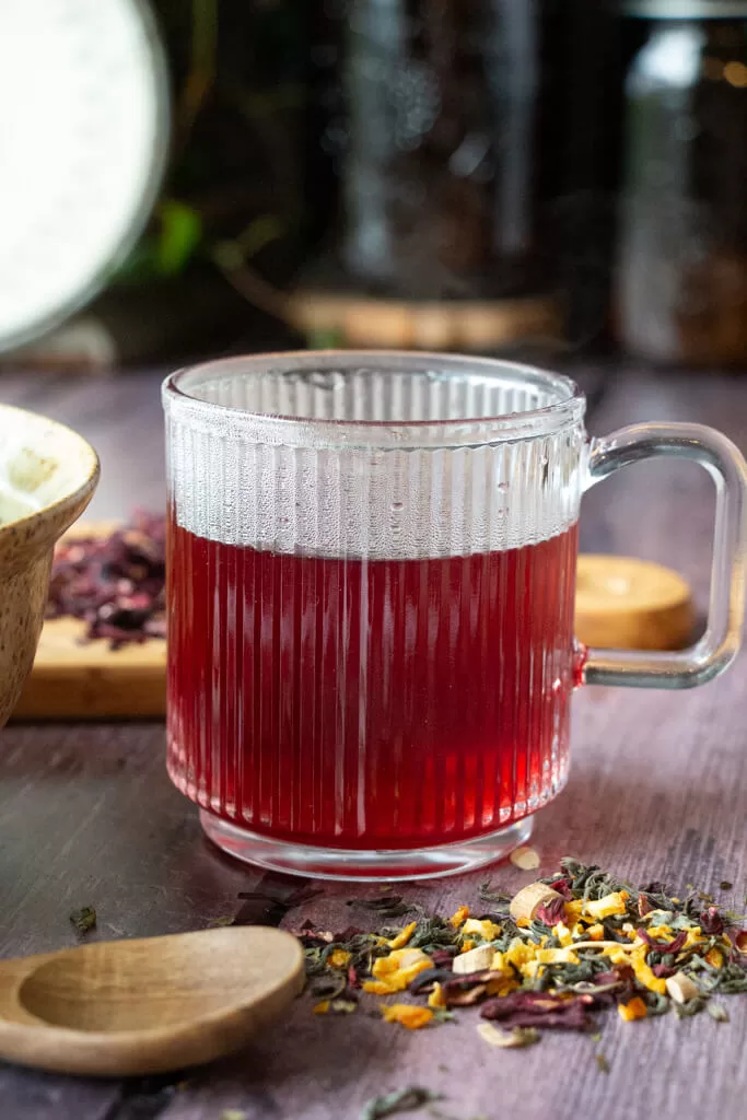herbal tea for energy- pink tea in clear mug surrounded by spilled herbs