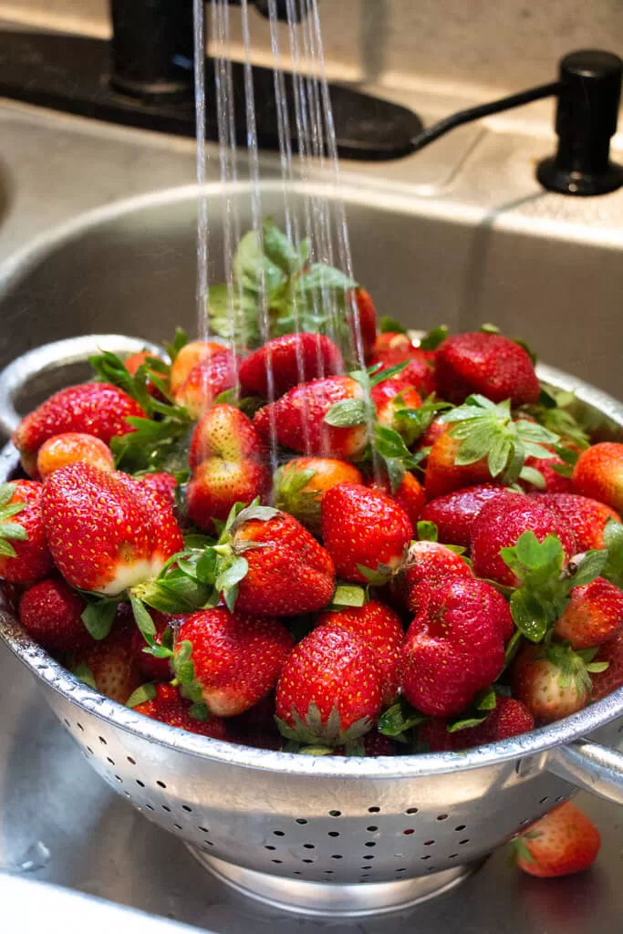 Washing strawberries in sink with metal strainer