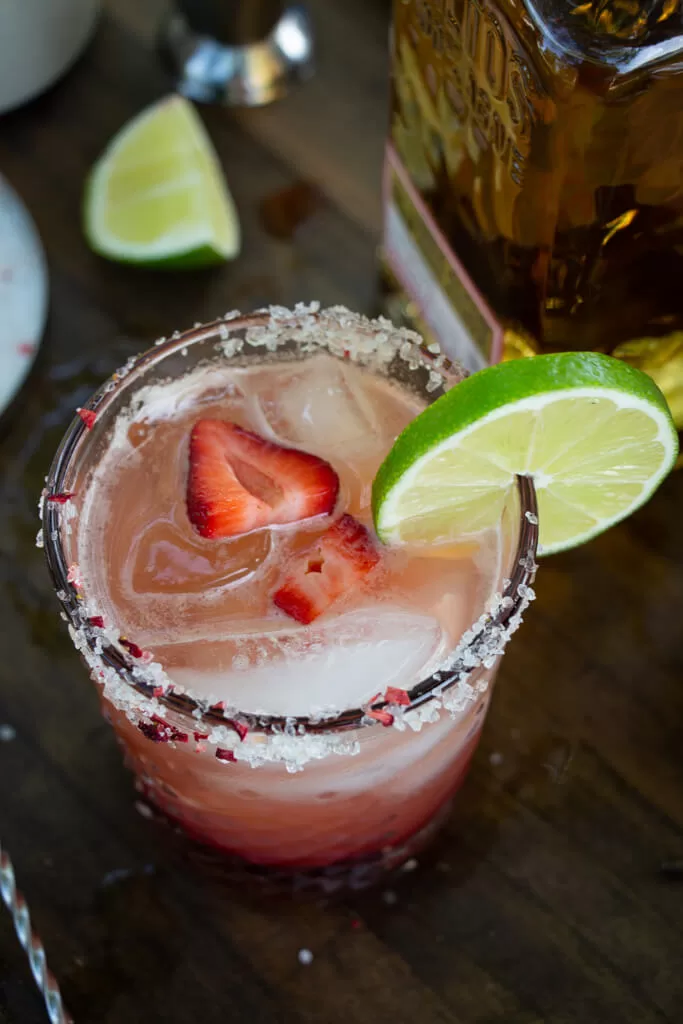 strawberry rose margarita from above in clear glass with strawberry and lime garnish