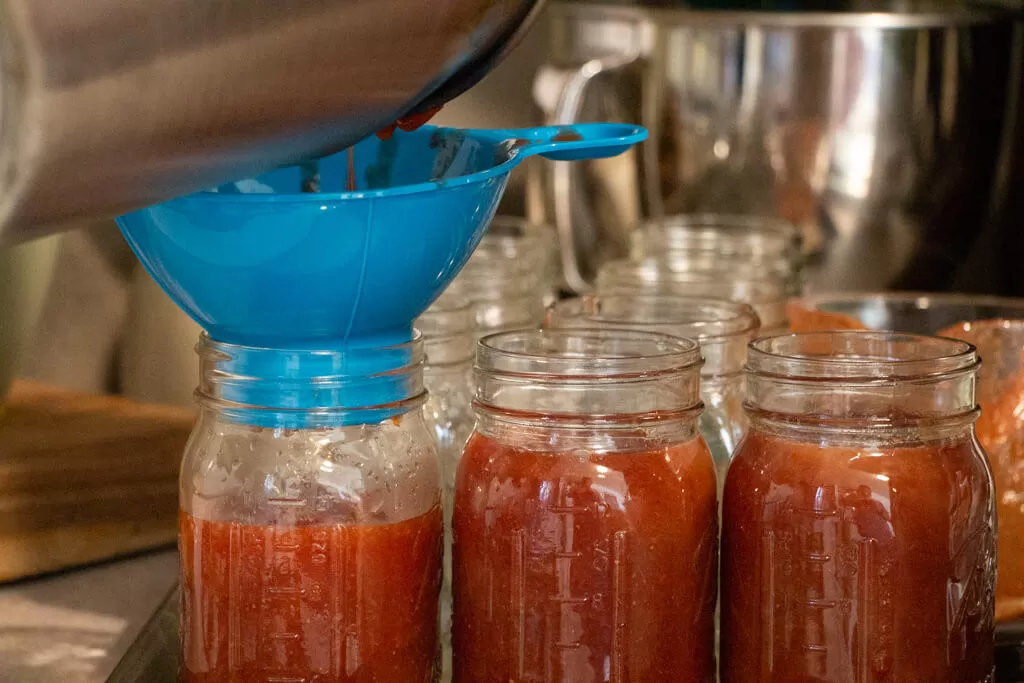 filling mason jars with blue funnel- several jars full of red jam