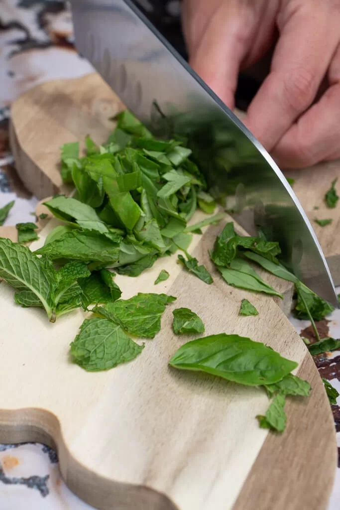 chopping basil with a big knife on a butterfly shaped wood cutting board
