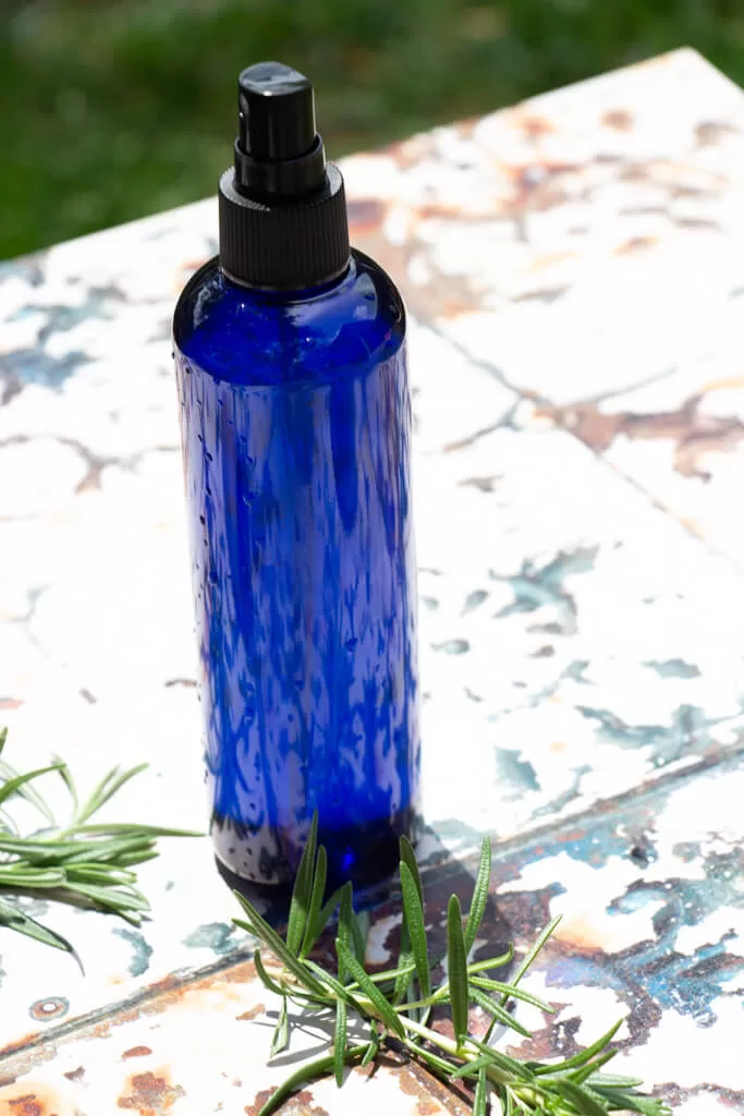 cobalt blue bottle of bug spray sitting on table with rosemary with rusted tin top