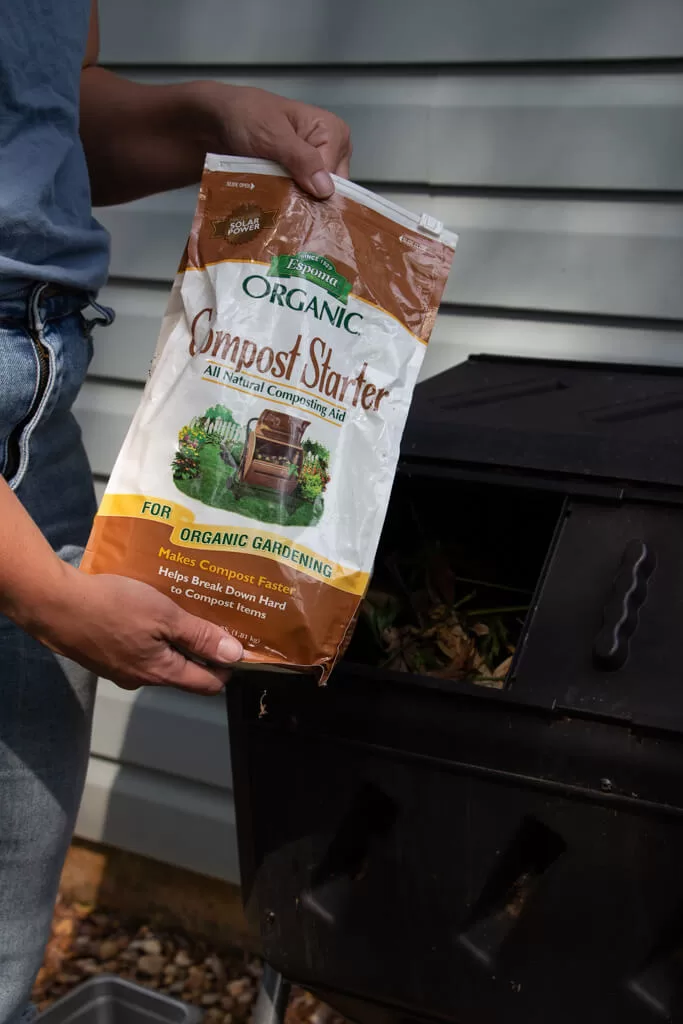 compost starter in a brown bag (holding it in front of a black compost tumbler)