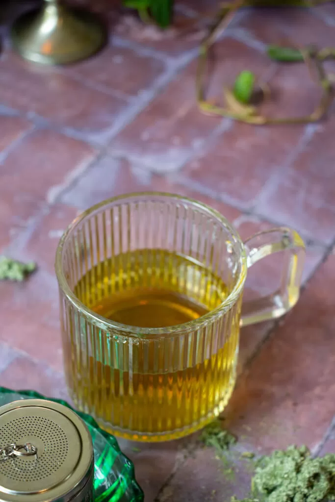 cup of light brown mugwort tea in a clear mug on a brick backdrop