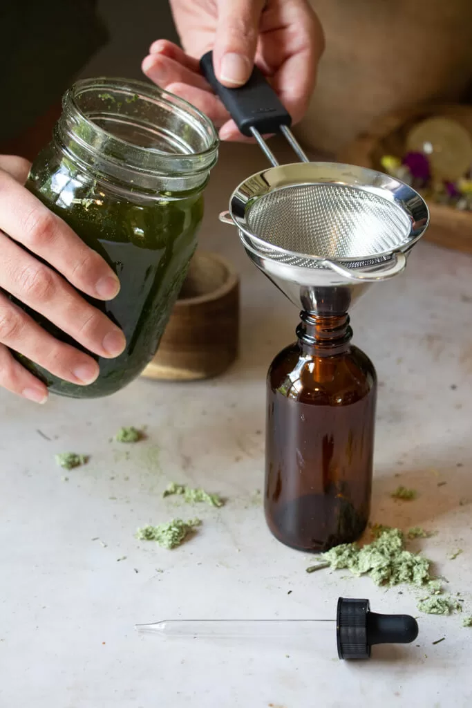 straining mugwort tincture into amber dropper bottle with mini funnel and strainer