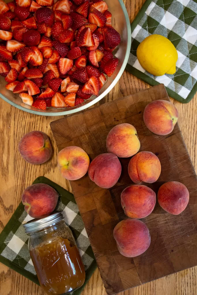 ingredients laid out on table- cut strawberries, whole peaches, a lemon, and a mason jar of honey