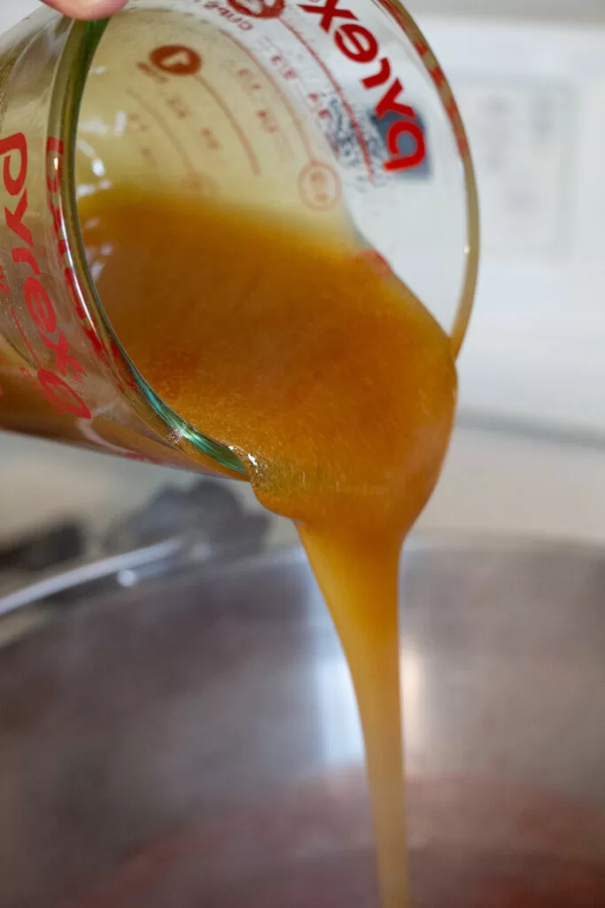 pouring honey and pectin mixture into pot with pyrex measuring cup