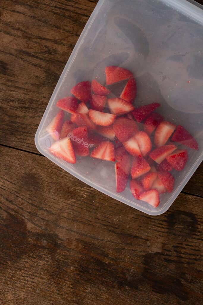 a clear silicones stasher bag full of cut strawberries sitting on a wood table