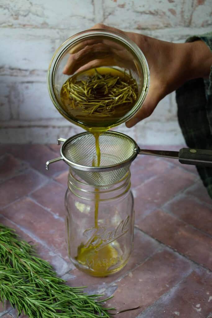 hand straining rosemary oil with mesh strainer