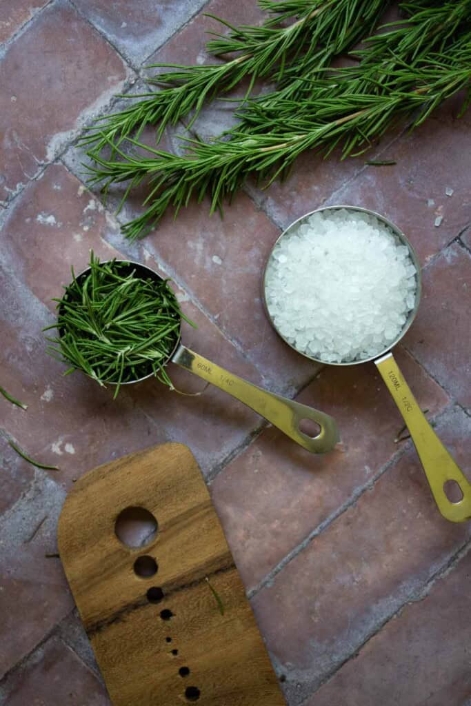 rosemary salt ingredients in measuring cups next to rosemary and herb stripper