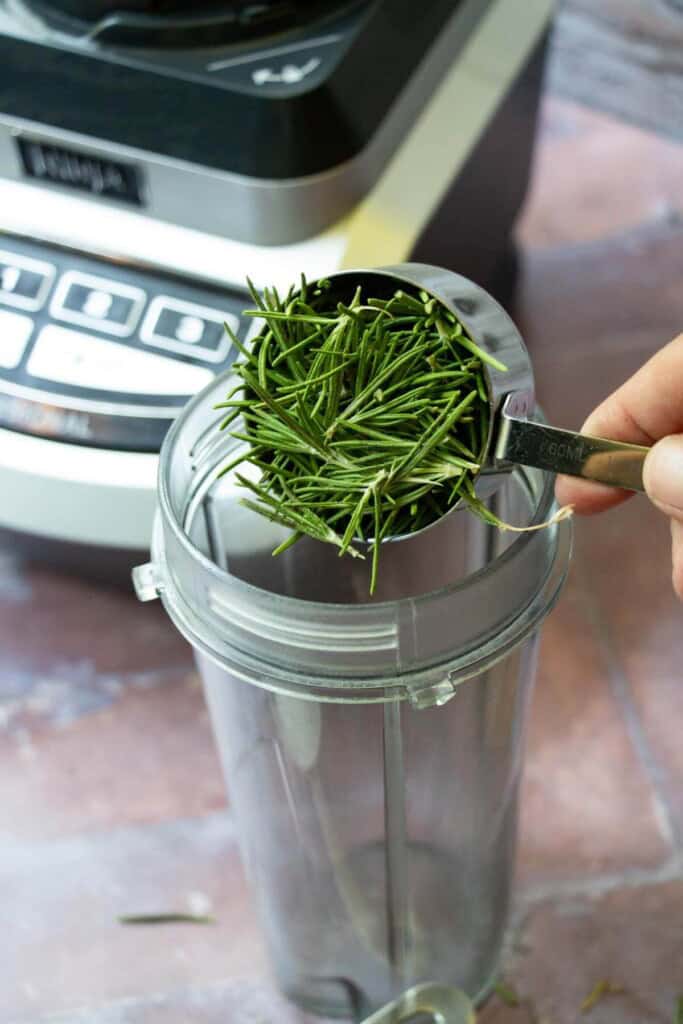 hand putting measured rosemary into blender cup