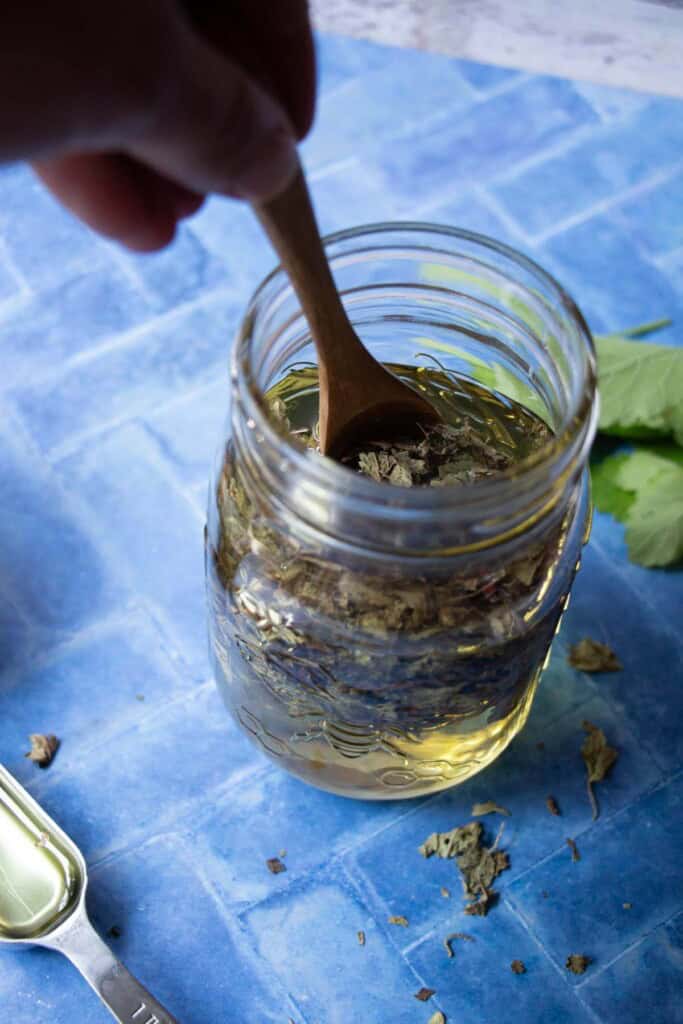 stirring lemon balm into oils with a wooden spoon