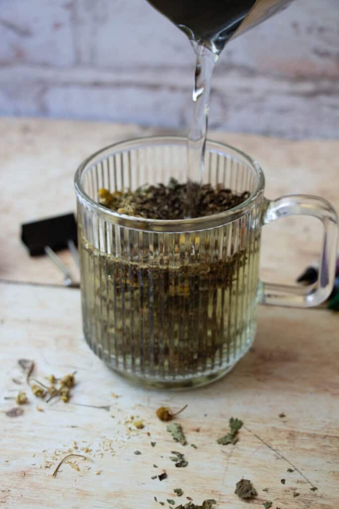 poring water over tea leaves in clear mug