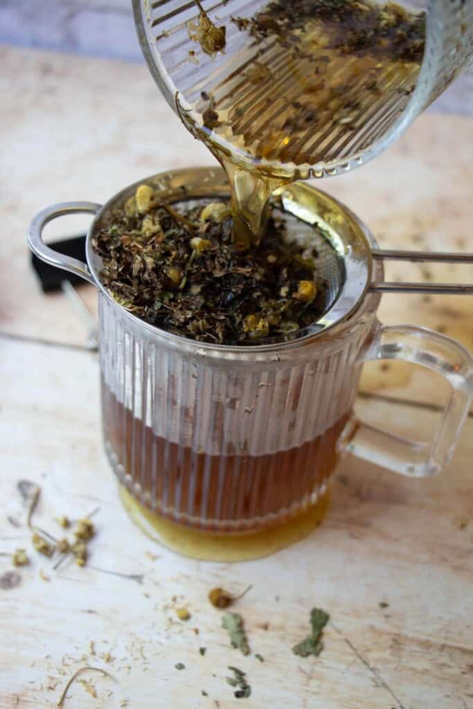 straining the herbal tea into a fresh mug