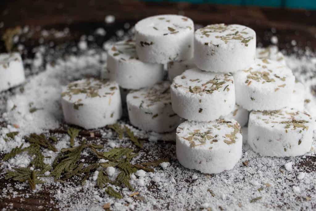 white shower steamers with dried herbs on top stacked on a table with ingredients all about