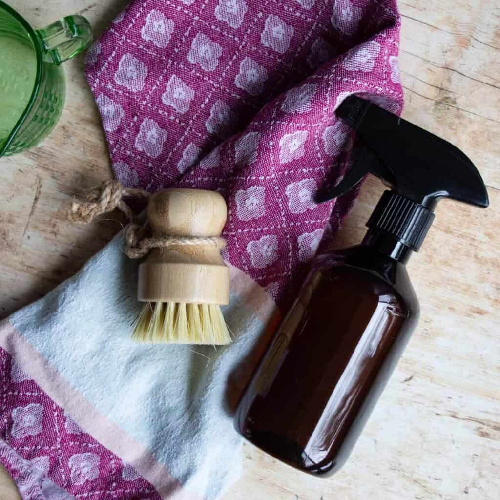 disinfectant spray in amber bottle with scrub brush and a colorful towel