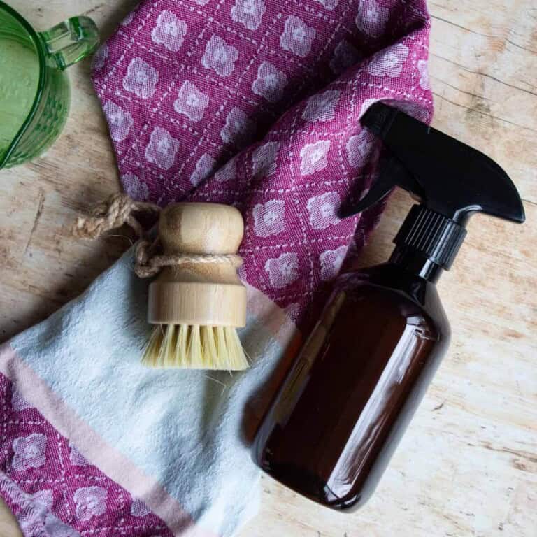 disinfectant spray in amber bottle with scrub brush and a colorful towel