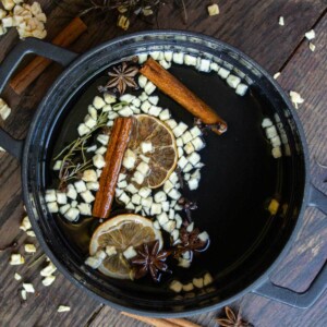 black pot on wood table with apples, oranges, cinnamon, cloves, and other simmer pot ingredients